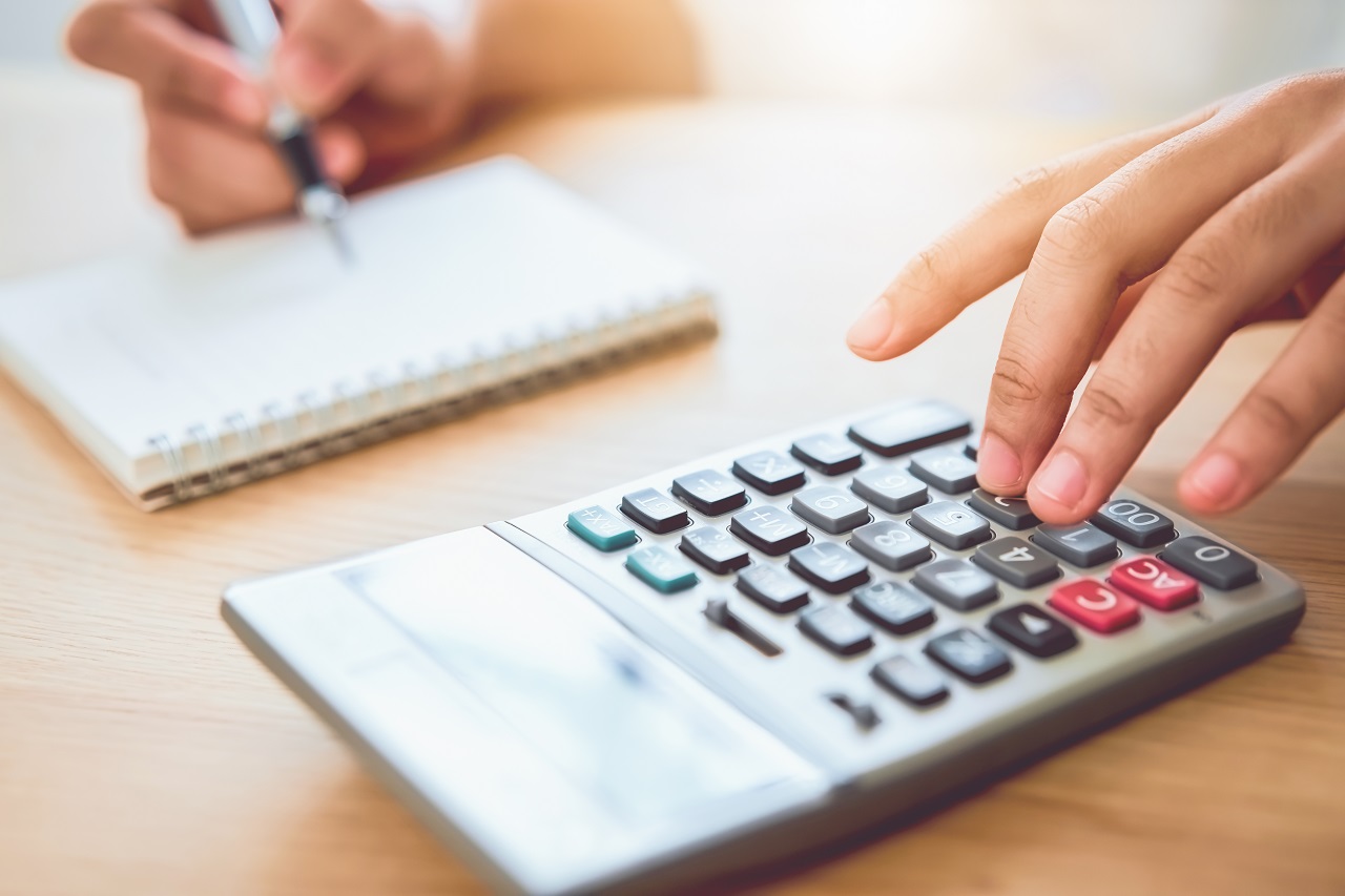 Close-up of a woman writing on a notebook while typing on a calculator