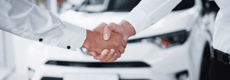 Two men shaking hands in front of white car