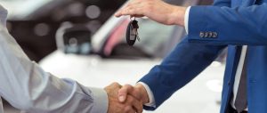 Two men shaking hands in front of a car