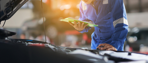 Asian auto mechanic man or Smith writing to the clipboard at workshop warehouse, technician doing the checklist for repair machine a car in the garage