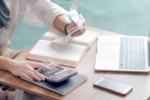 Closeup young woman calculating accounting budget, holding a receipt using calculator and sitting on sofa in the living room.