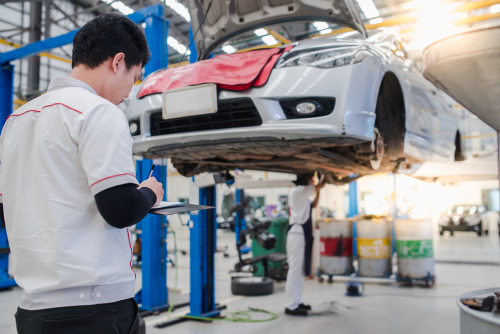 A mechanic stands in front of a car in a car shop, writing things down on a clipboard. This is to illustrate the article's discussion of cars with the best resale value.