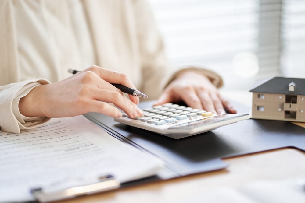 Closeup of a woman's hands holding a pen and pushing buttons on a calculator. This relates to the topic of how to improve one's chances of getting a loan.